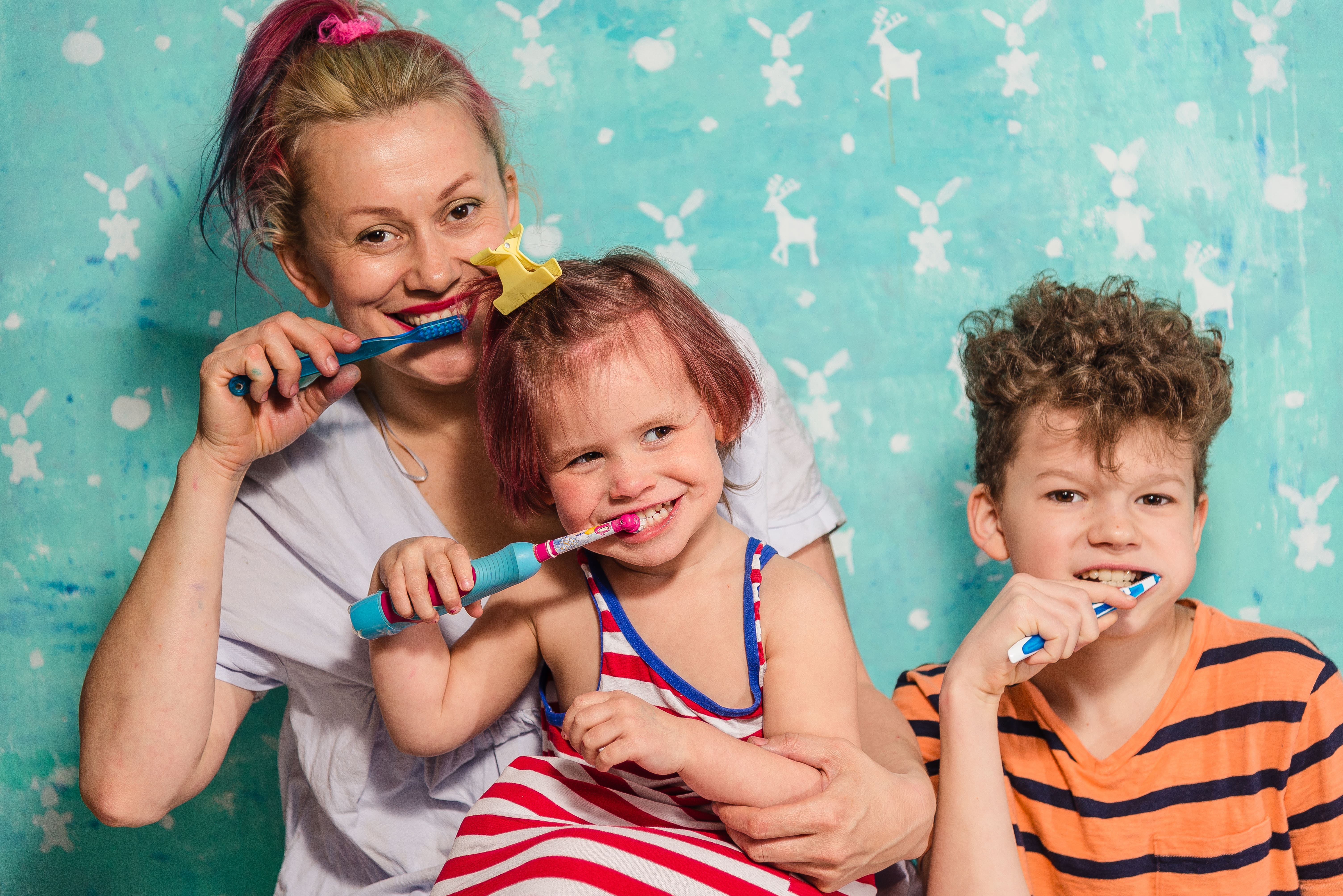 Brother and sister happily brushing their teeth with mother on a blue background